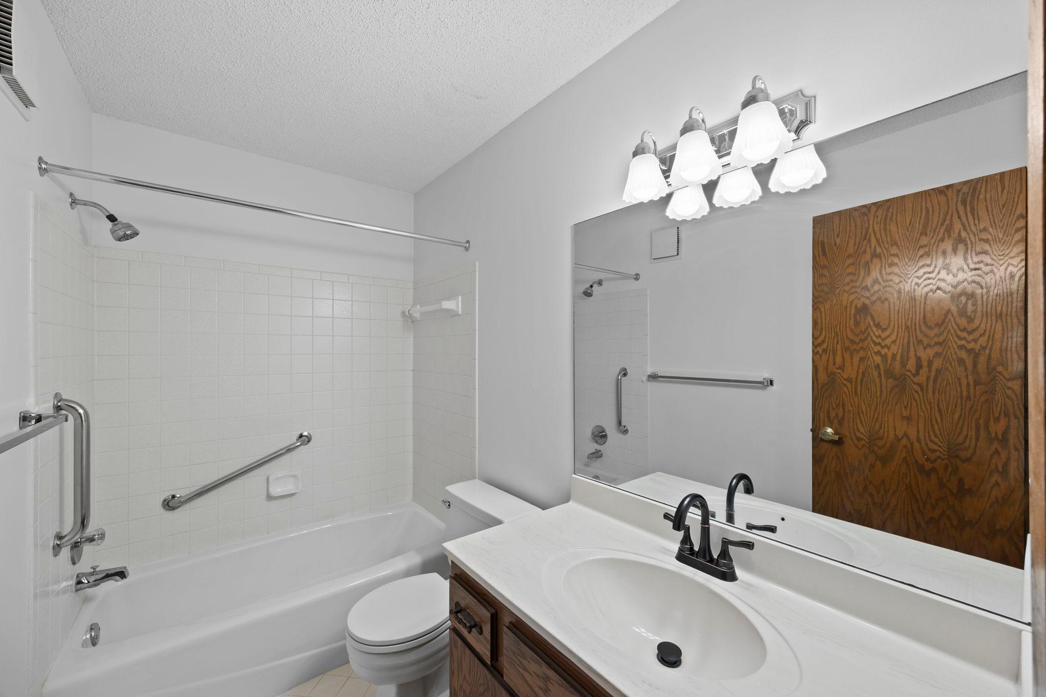 A nearby full bathroom offers a tiled tub and shower combination, tile flooring, a vanity with built-in storage, and additional hall cabinetry for extra convenience.