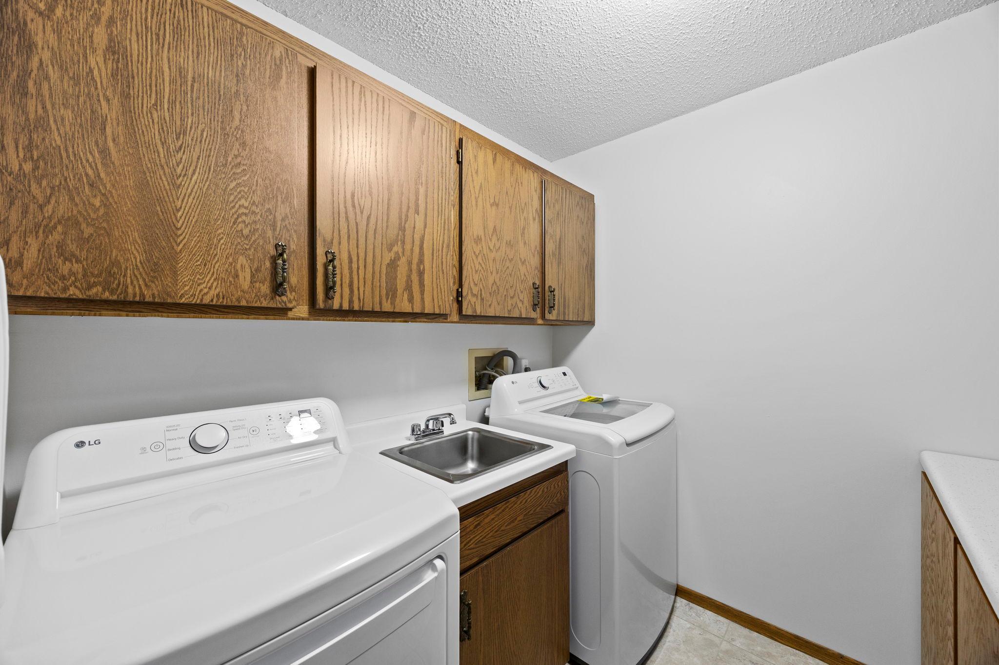 The dedicated in-unit laundry space features tile flooring, an LG washer and dryer, a utility sink, and generous cabinetry for storage and organization.