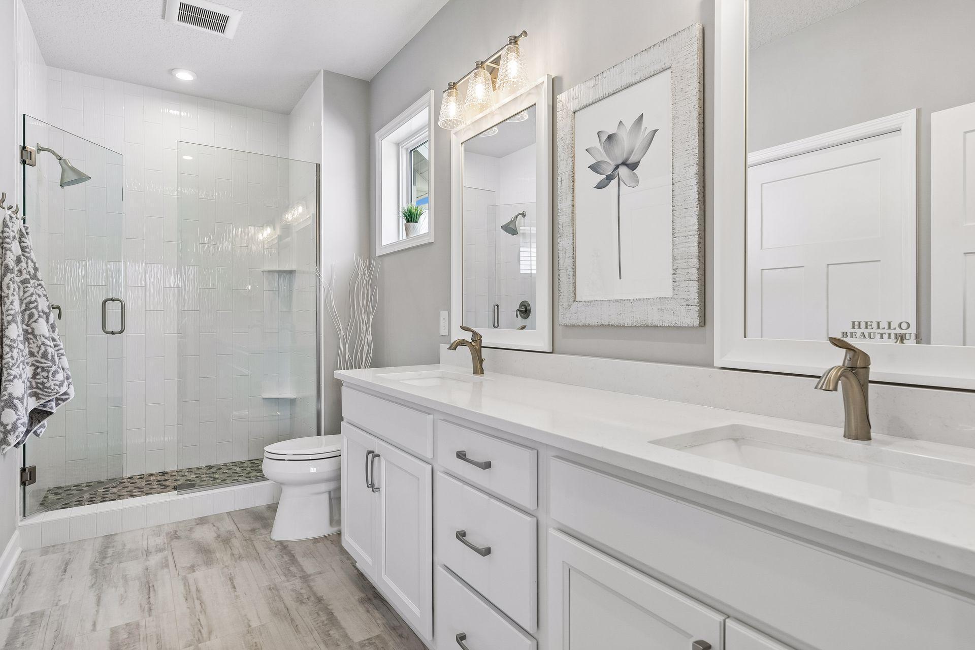 Primary bath with double sinks, new framed mirrors, fully tiled shower and frameless glass shower door.