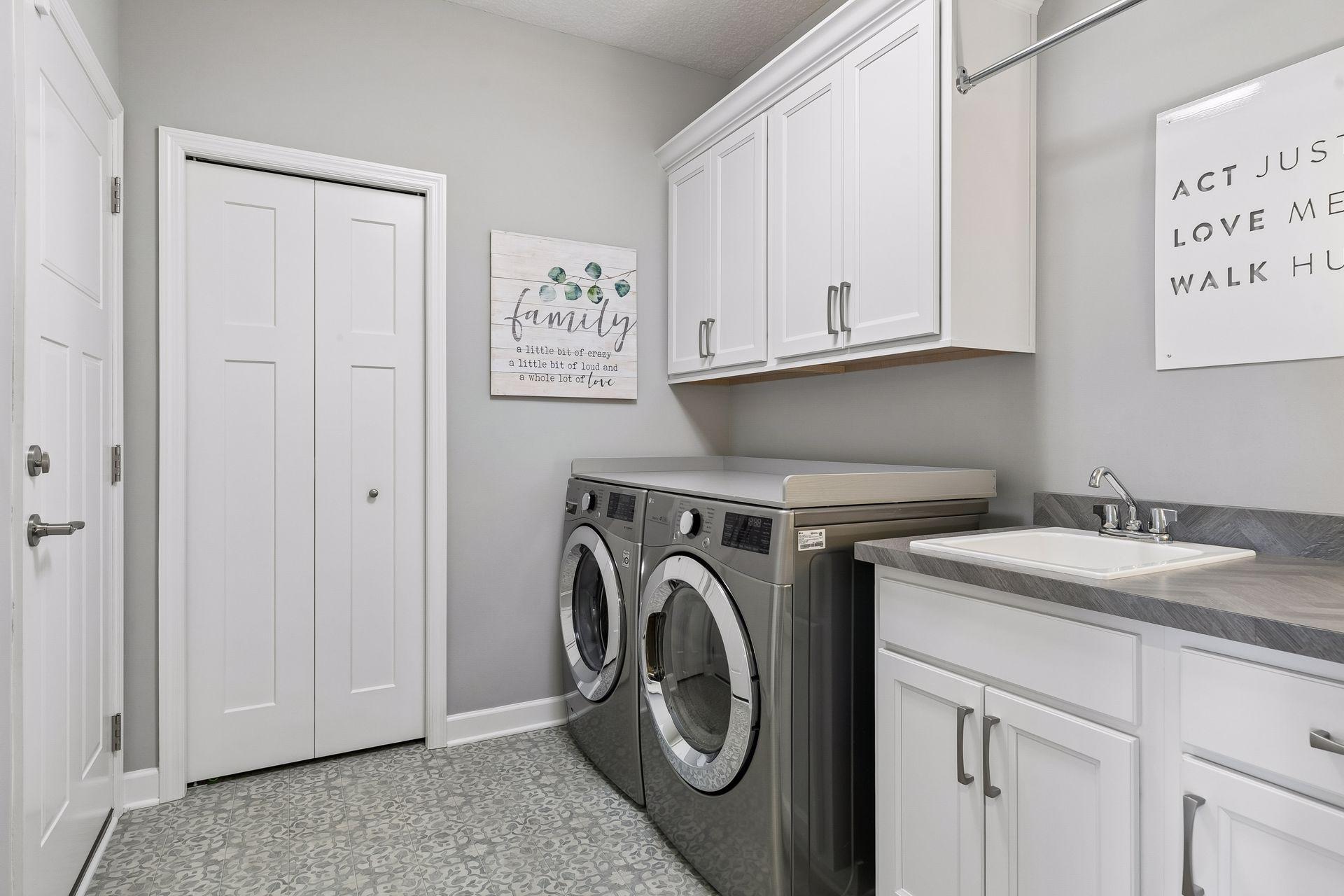 Laundry room with overhead cabinets, drying rod, utility sink with base cabinet and folding counter over washer/dryer.