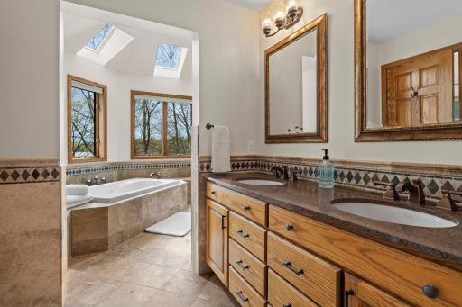 Features a soaking tub, expansive tiled walk-in shower, dual vanity, tile flooring and wainscoting.