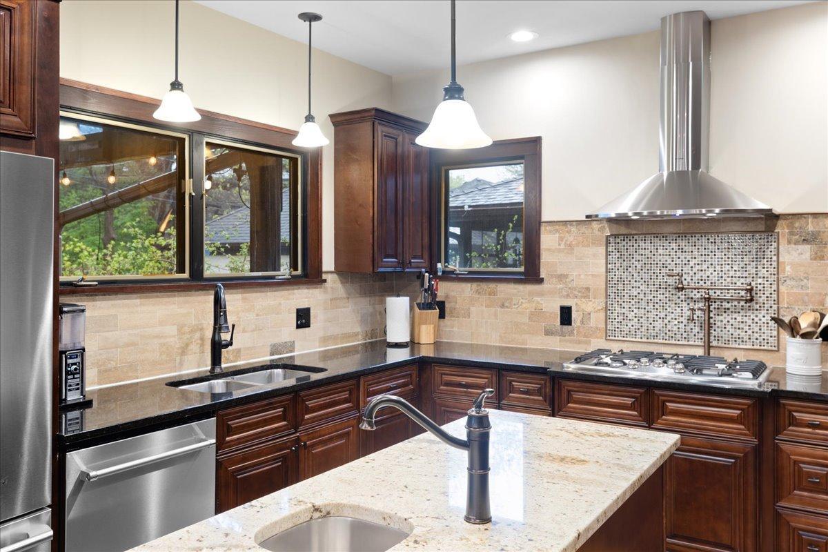 Warm, upscale kitchen with rich wood cabinetry, granite countertops, stainless steel appliances, and a statement range hood.