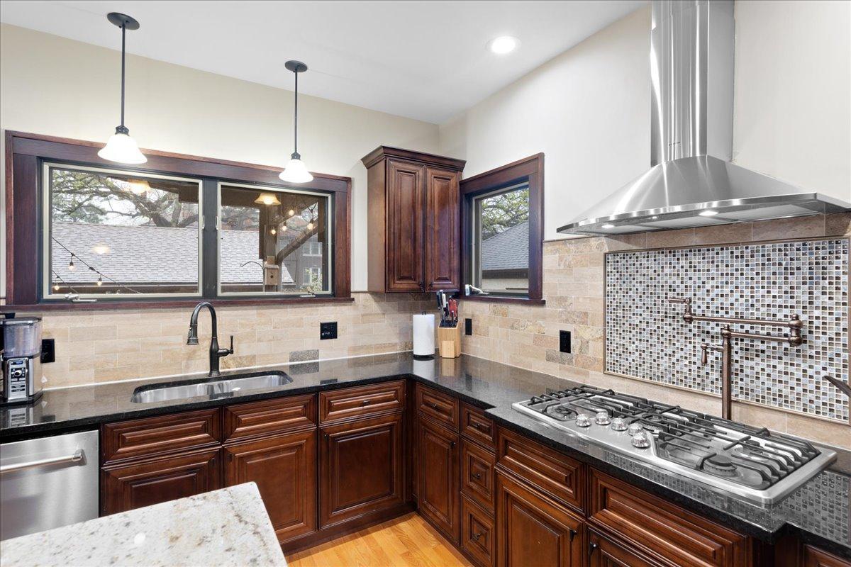 Chef-inspired kitchen with custom cabinetry, granite countertops, stainless steel range hood, pot filler, and stylish tile backsplash.