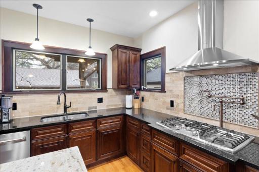 Chef-inspired kitchen with custom cabinetry, granite countertops, stainless steel range hood, pot filler, and stylish tile backsplash.