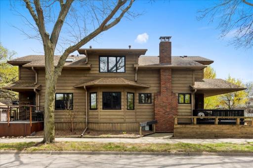 Side elevation showcases the homeâs timeless character with classic wood siding, updated windows, and brick chimney, offering a clean, well-maintained exterior with mature tree coverage for added charm and shade.