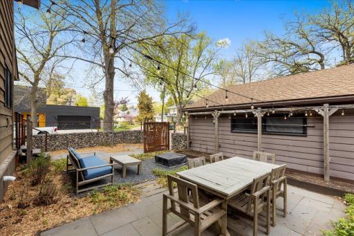 Beautifully designed outdoor living space featuring a private, enclosed patio with custom stone wall, dining area, and lounge space. Complete with string lighting for the perfect ambiance to relax or entertain.