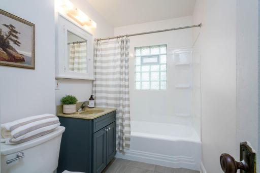 Main level bathroom features a new toilet, block window, new vanity, and a refinished tub with updated tub surround.
