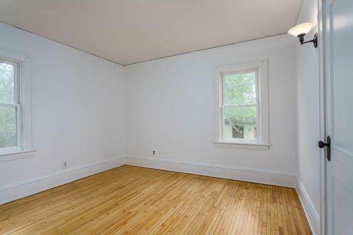 Second generously sized main-floor bedroom featuring windows on two sides and gleaming hardwood floors.