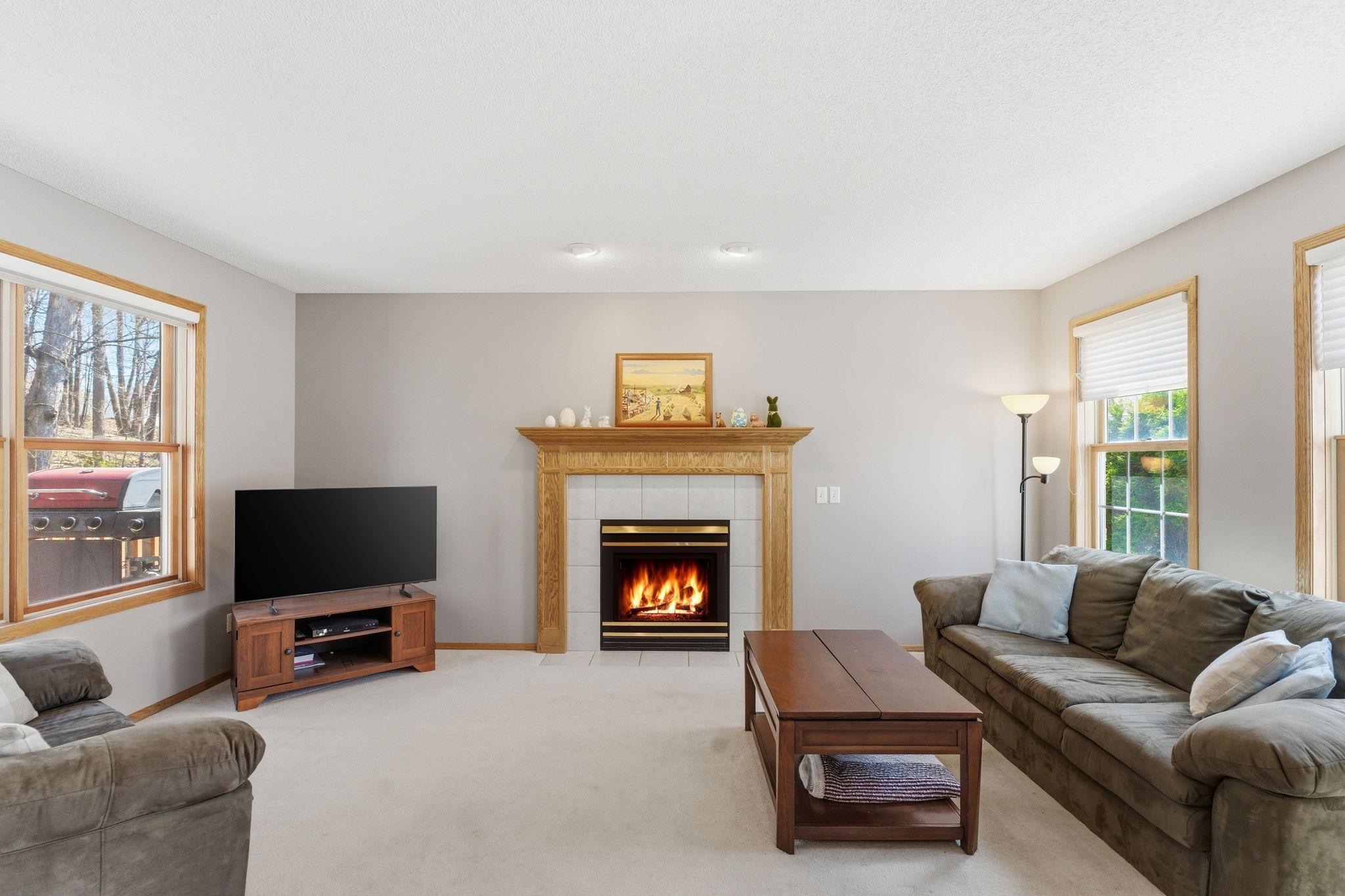 Main level living room with gas fireplace is filled with natural lights from windows with views of both the front and back yards of the home.