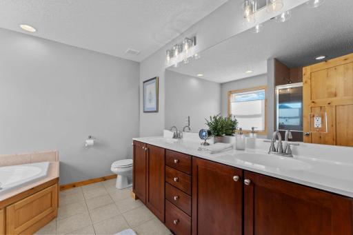 The private ensuite bathroom offers a spa-like retreat with a jetted soaking tub, walk-in shower, dual-sink vanity, and tile flooring.
