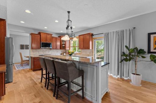 The beautifully appointed kitchen features abundant warm wood cabinetry, granite countertops, and a spacious two-tier center island with breakfast bar seating.