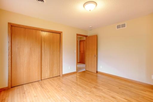 Warm hardwood flooring and oversized windows create an inviting and cheerful bedroom retreat.