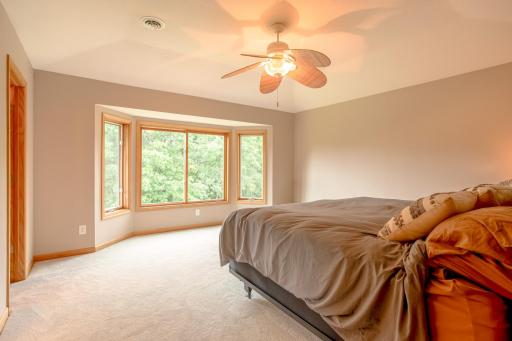 Expansive primary bedroom offers a peaceful retreat with vaulted ceilings and a large bay window overlooking mature trees.