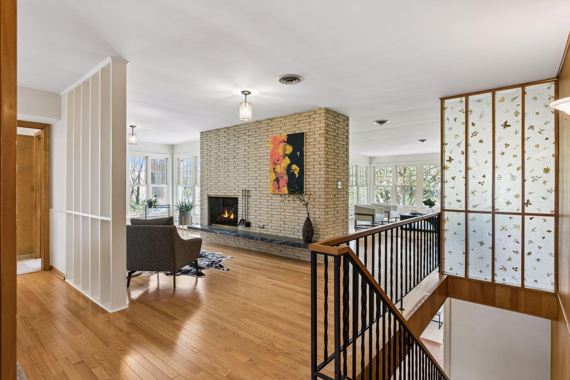 The open floorplan is bright and airy with an open stairway, fun vintage screen, gleaming hardwood floors, oversized windows and it is anchored by the full wall double sided brick fireplace.