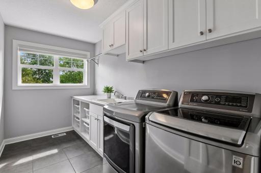 Upstairs laundry room with upper cabinetry, base cabinetry, countertop folding surface, and service sink.
