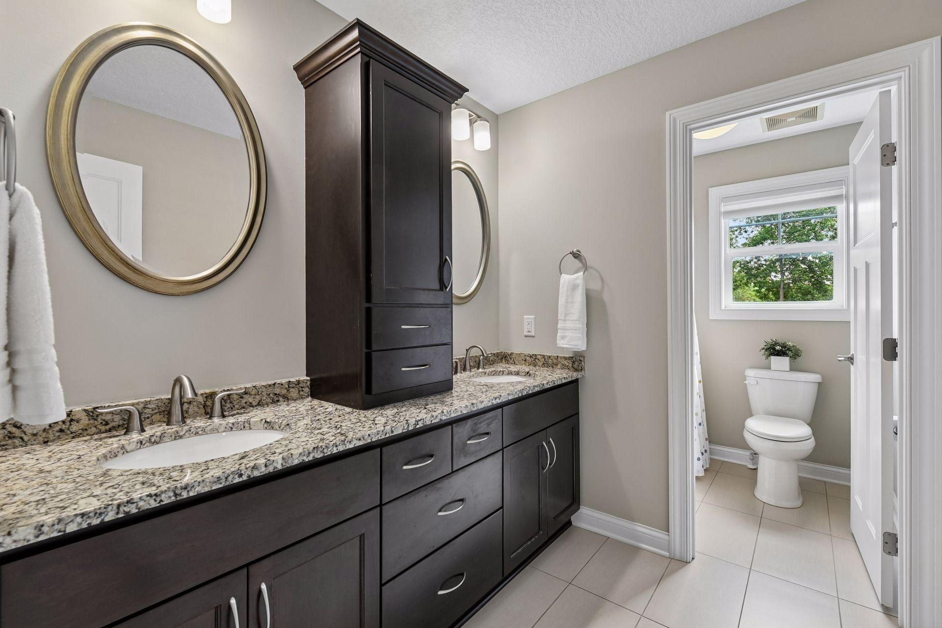 Full bath with double vanity, granite countertop, center cabinetry tower, and separate water closet and shower.
