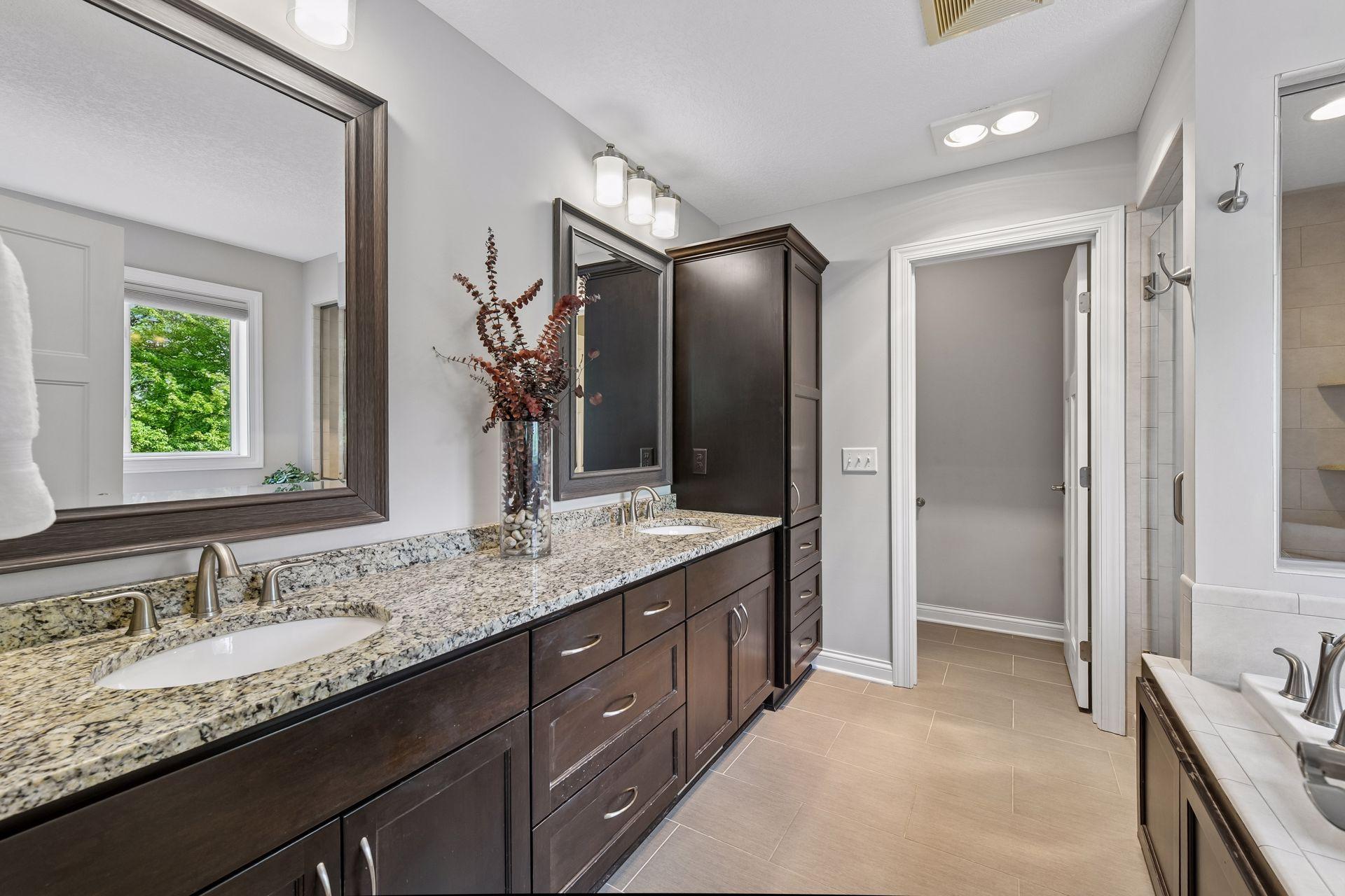 Primary bath with double vanity, granite countertop, framed mirrors, and linen cabinet storage