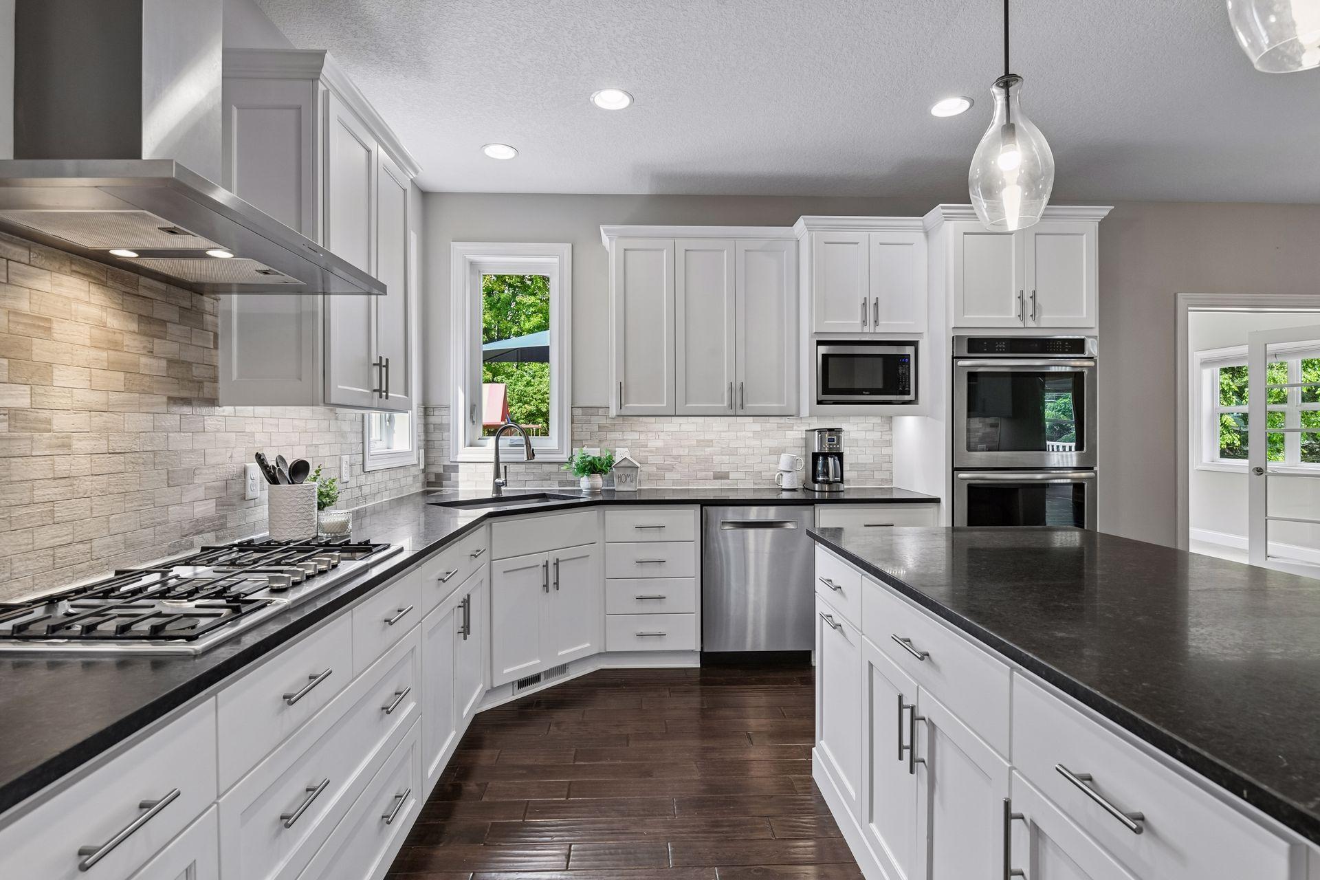 Kitchen with gas range, double wall ovens and built-in microwave, dishwasher, and corner window over sink to provide natural light.