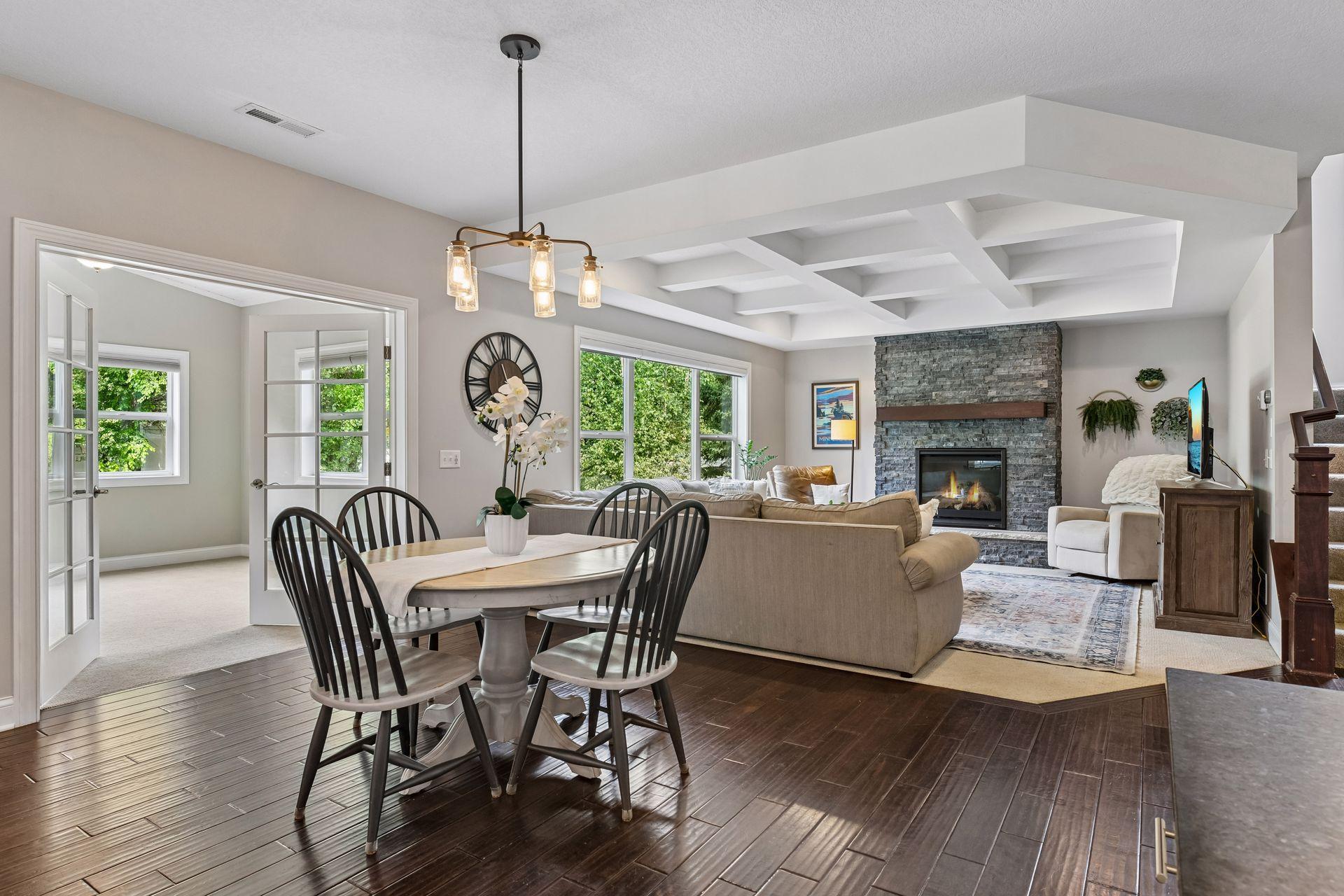 Informal dining area open to living space with coffered ceiling and stone-surround fireplace beyond