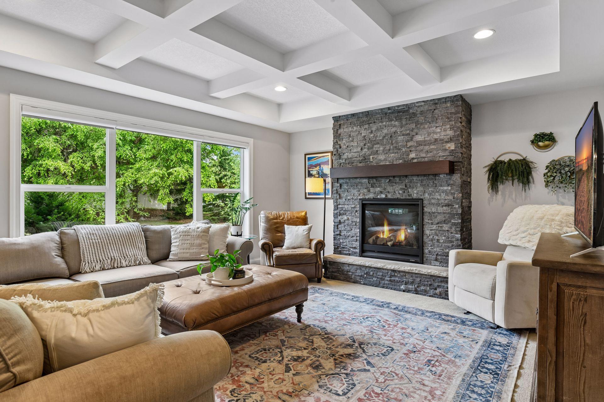 Living area with coffered ceiling, stone-surround fireplace with raised hearth and wood mantel, and oversized windows