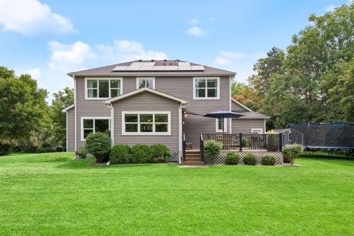 Back of home with raised deck, walkout access, and mature landscaping
