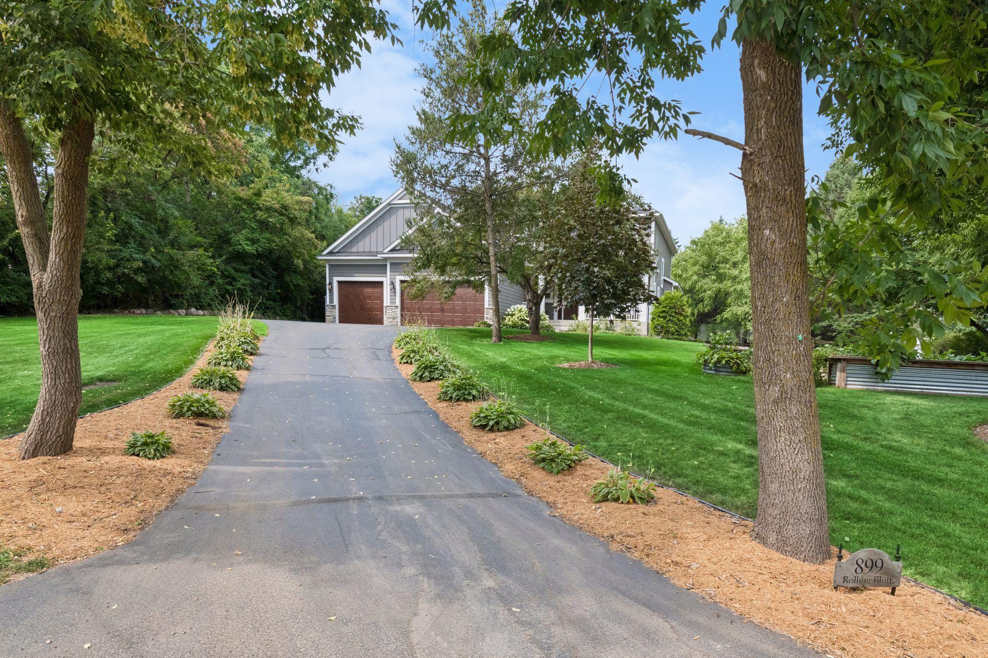 Paved private drive approaching attached three car garage with mature tree canopy and landscaped border beds