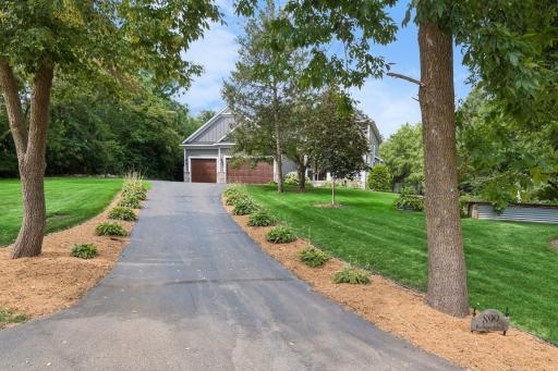 Paved private drive approaching attached three car garage with mature tree canopy and landscaped border beds