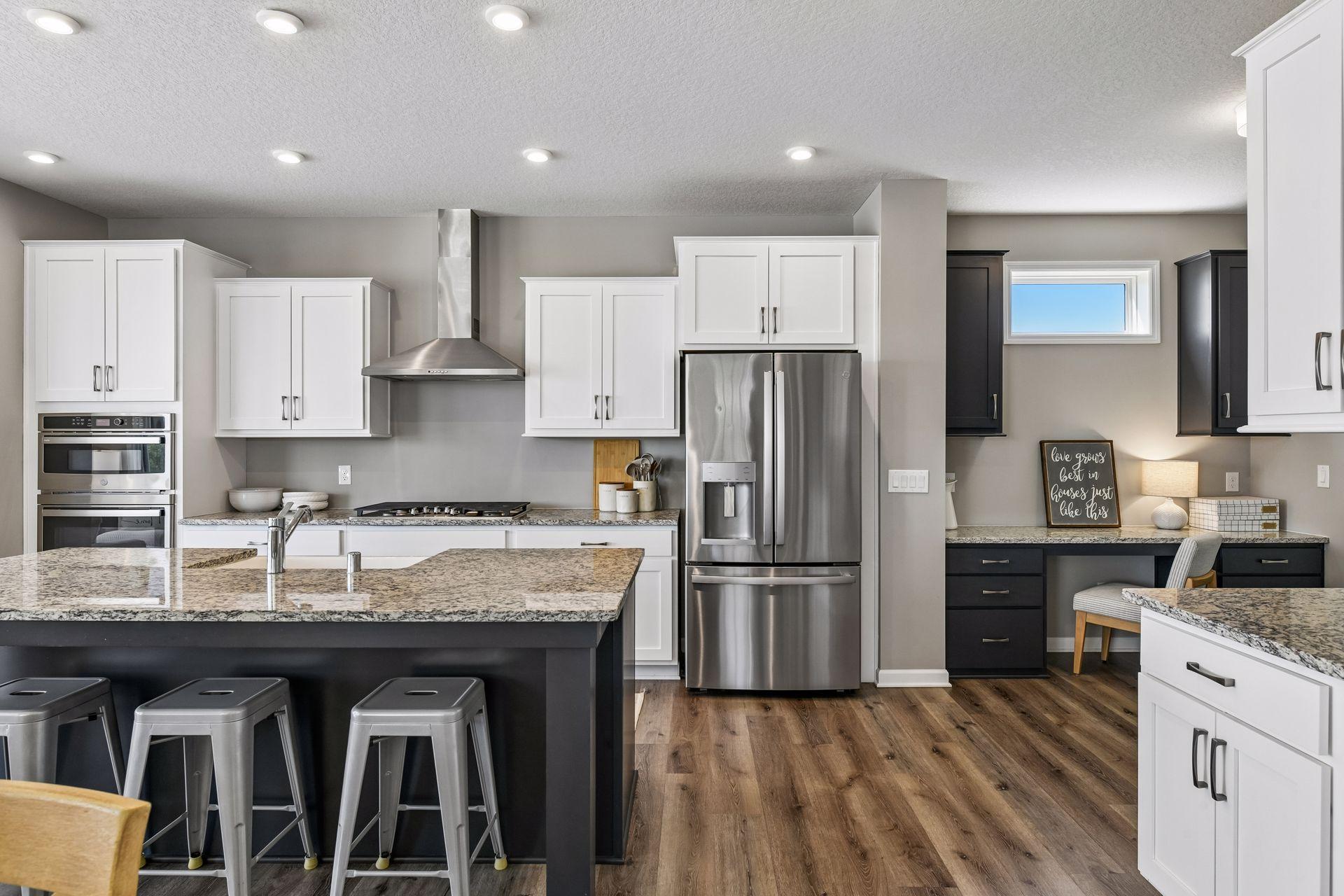 Built-in tech nook with contrast cabinetry and granite countertops, tucked just off the chef's kitchen with wall ovens, gas range, and French door refrigerator.