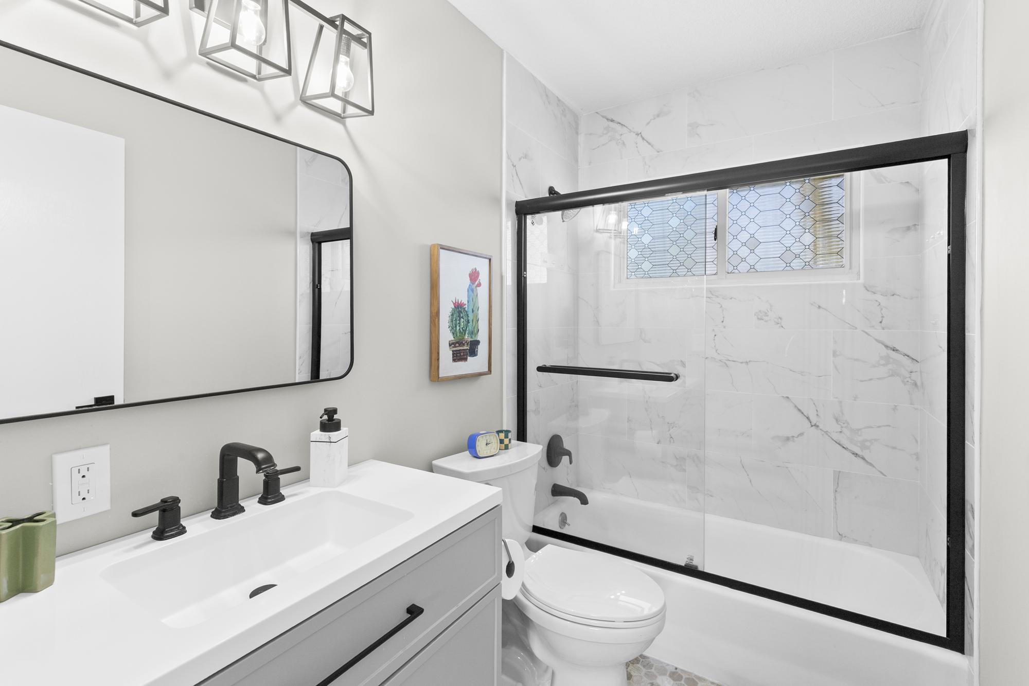 The beautifully updated main-floor bathroom features a clean white vanity, modern lighting, and a gorgeous tiled shower surround.
