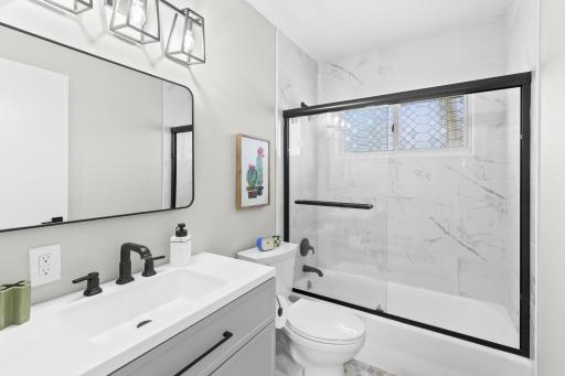 The beautifully updated main-floor bathroom features a clean white vanity, modern lighting, and a gorgeous tiled shower surround.