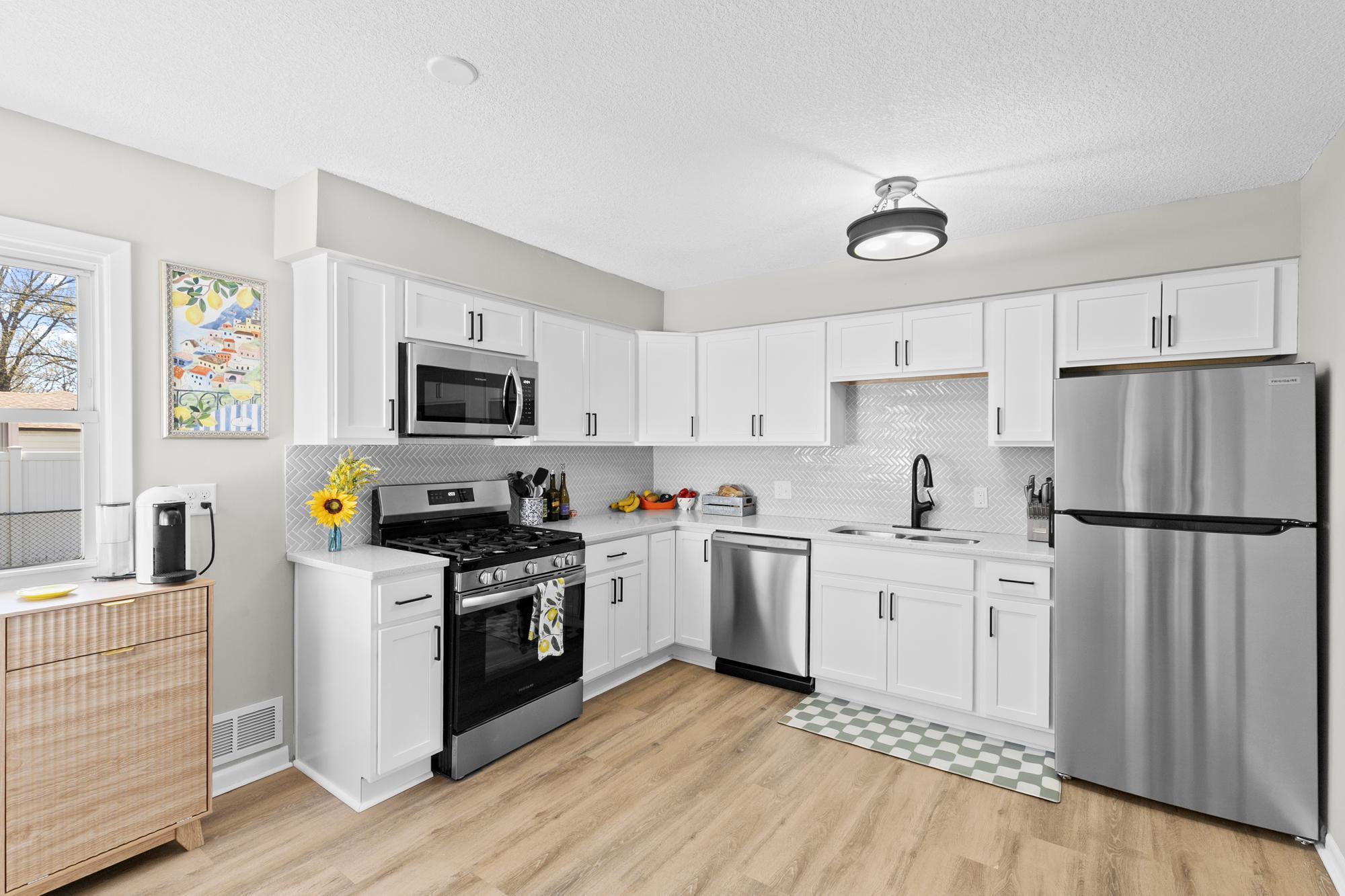 A stunning, fully updated kitchen featuring gorgeous stone countertops, crisp new cabinetry with modern hardware, and a full suite of stainless steel appliances including a gas range.