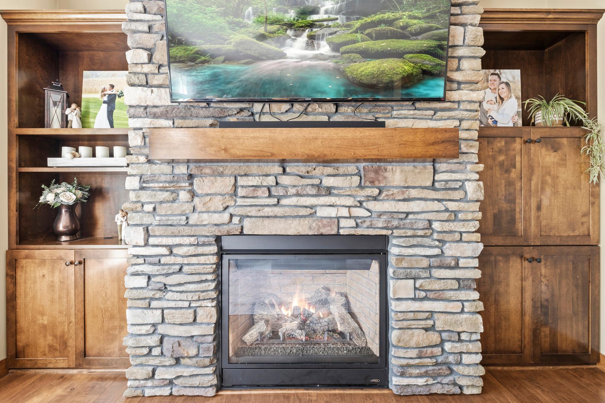 Custom gas fireplace wrapped in stone with a maple mantle