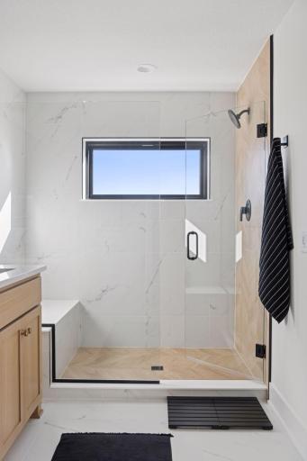 Primary bathroom ceramic shower with bench and frameless shower door.