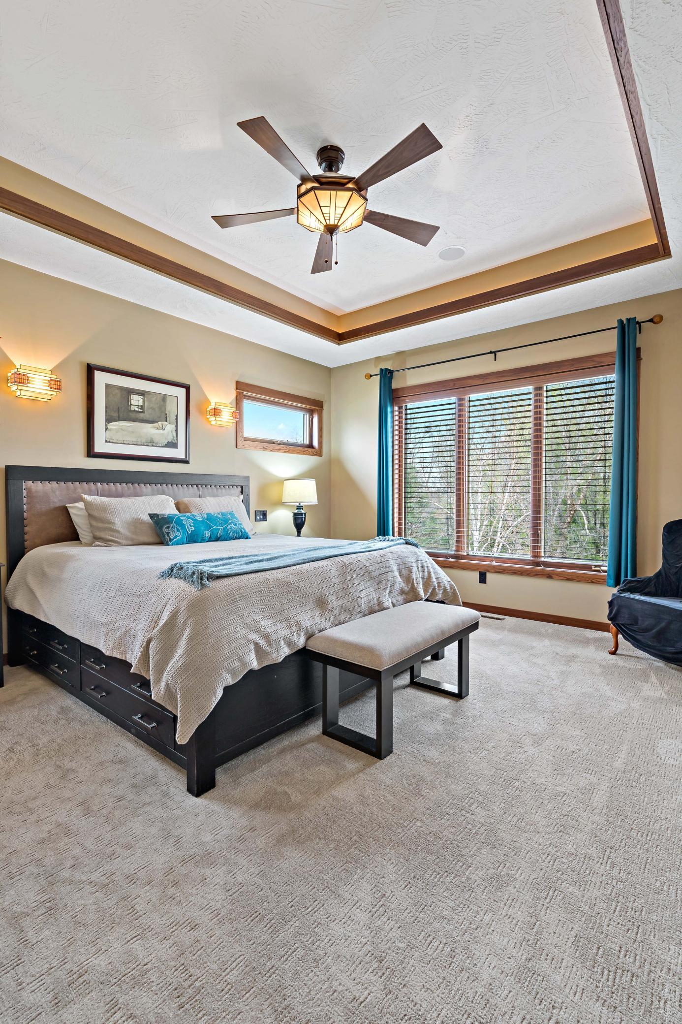 The main level Primary suite features a tray vaulted ceiling with both accent lighting and crown molding. The windows overlook the backyard trees and landscaping.