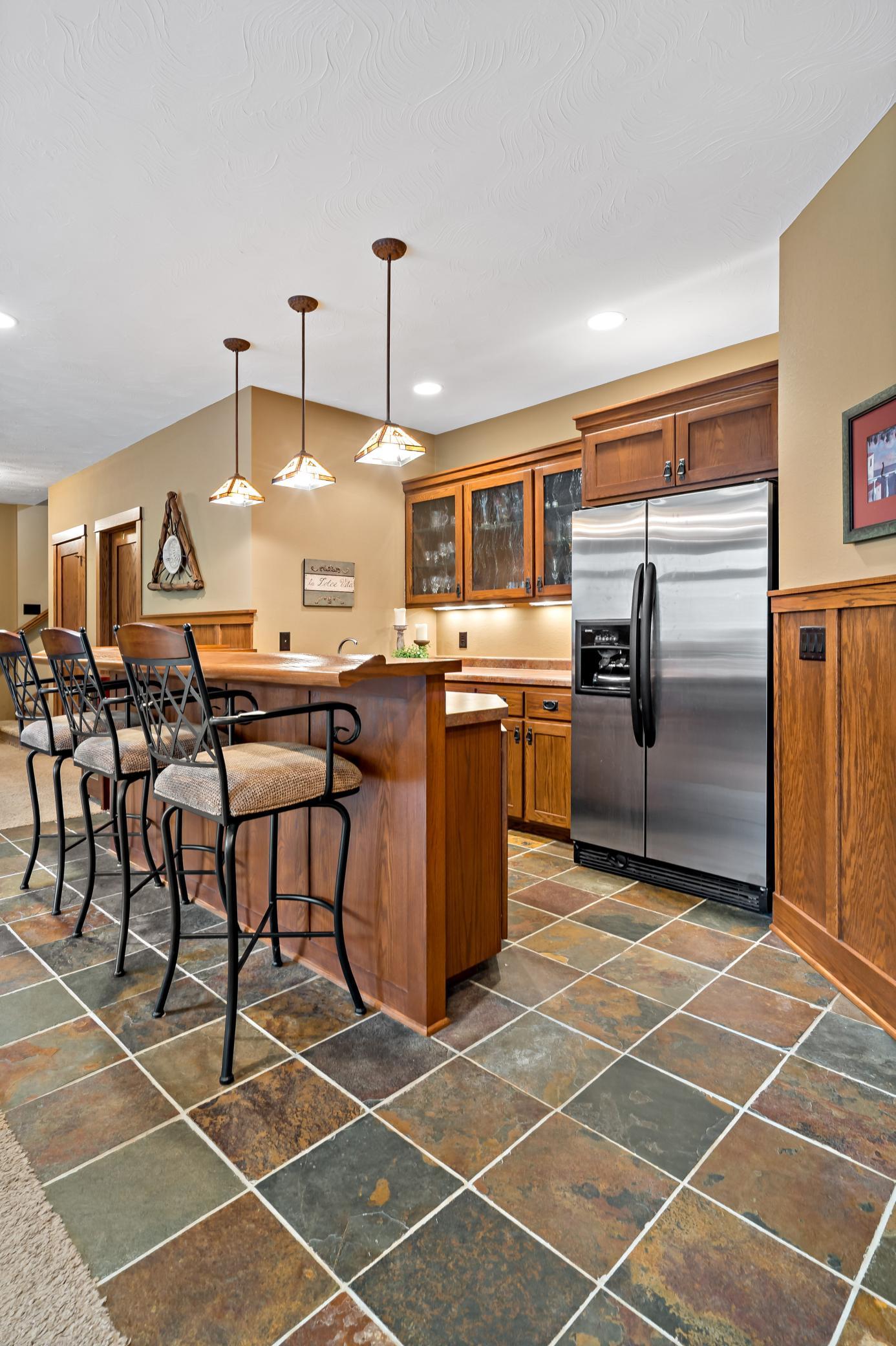 Mission style walk behind bar offers super cool pendant lighting, ceramic tile flooring, full sized refrigerator, and abundant storage.