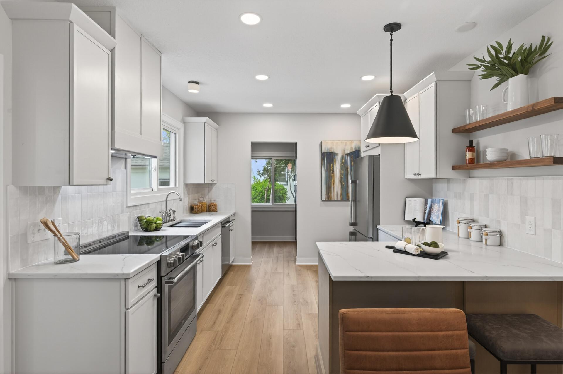 The fully renovated kitchen blends style and function with quartz countertops, new cabinetry, tile backsplash, and a peninsula with breakfast bar seating,