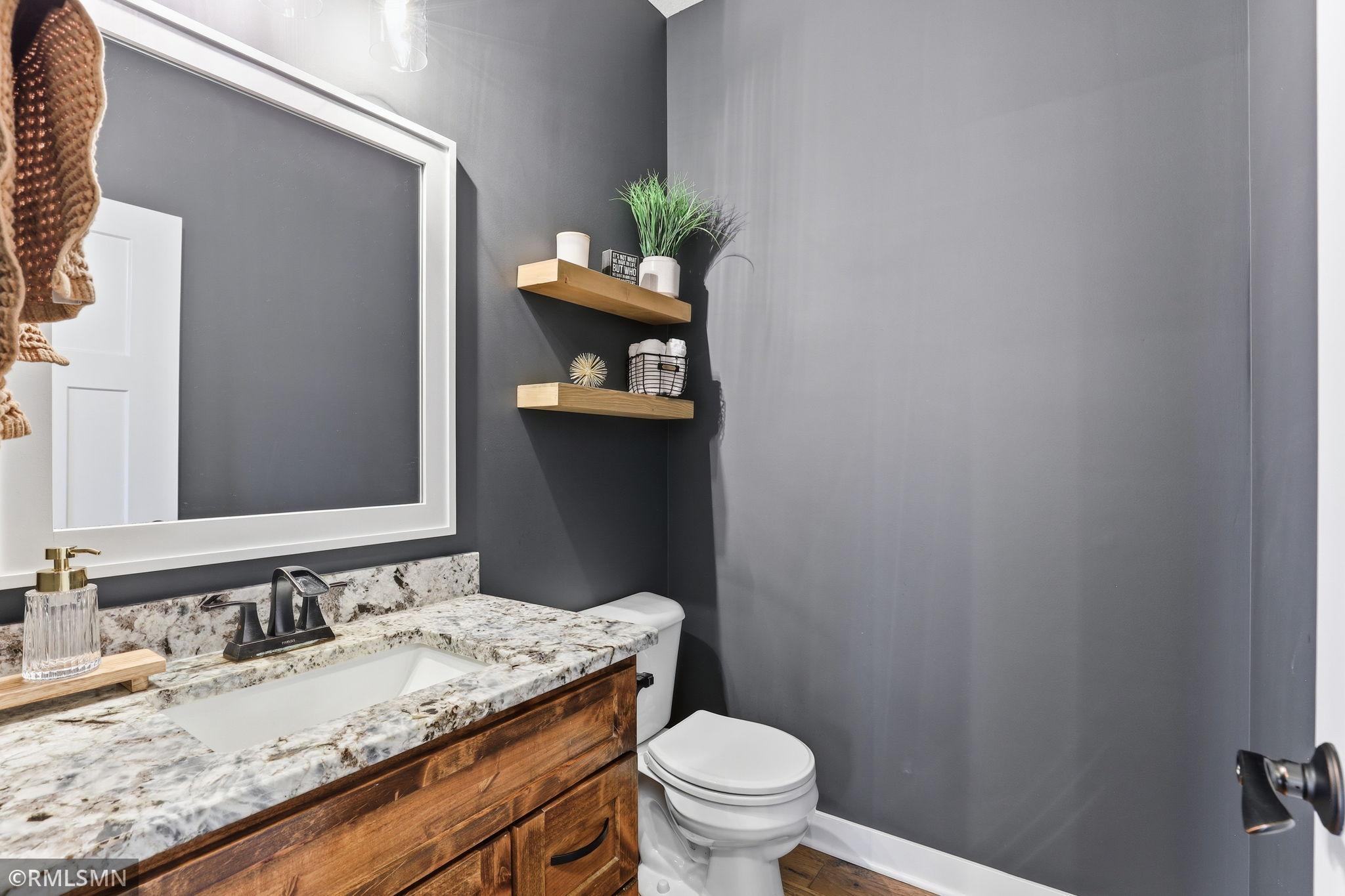 Convenient main floor half bath featuring granite countertops, warm wood cabinetry, and modern finishes. Perfect for guests and everyday use, offering both style and functionality.