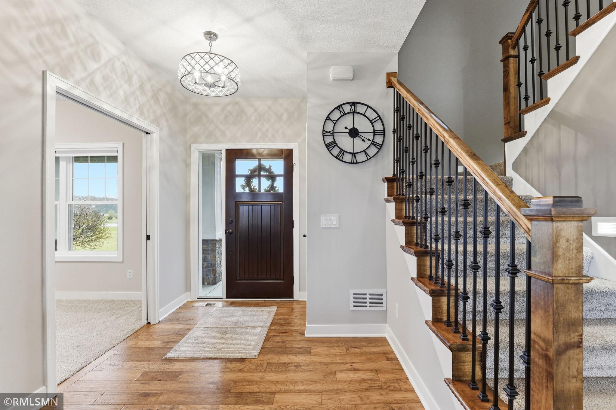 Bright and welcoming foyer featuring hardwood floors, stylish lighting, and a beautifully crafted staircase. A warm first impression with easy access to a main floor office or flex space.
