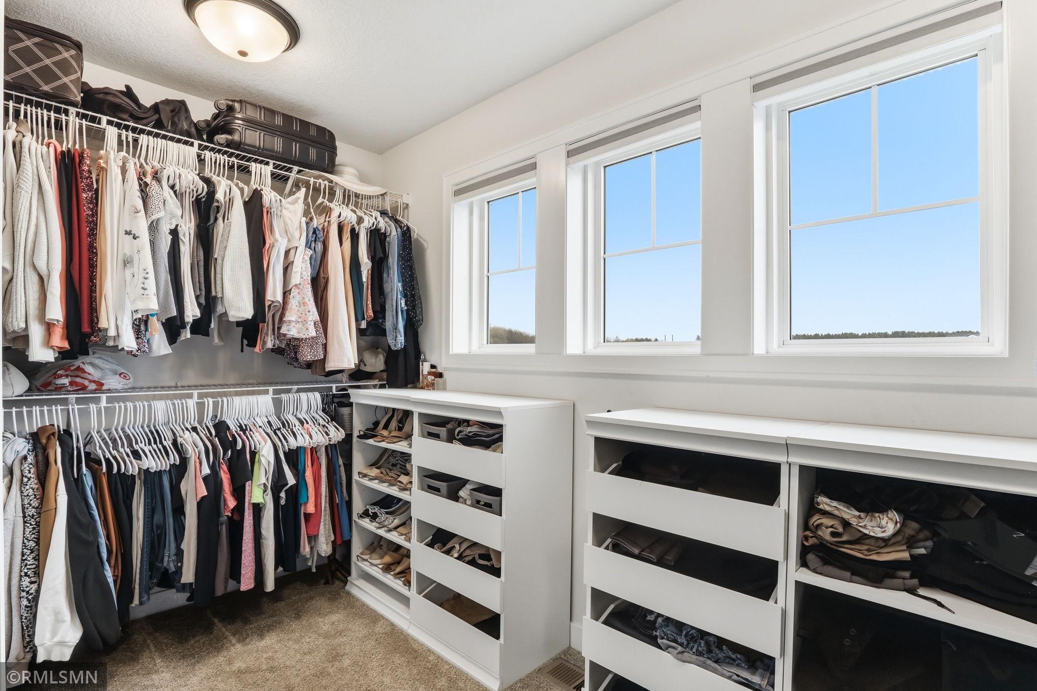 Organize with ease in this spacious walk-in closet featuring custom shelving, drawers, and abundant hanging space. Sort, store, and enjoy natural light from the windows as you get ready each day.