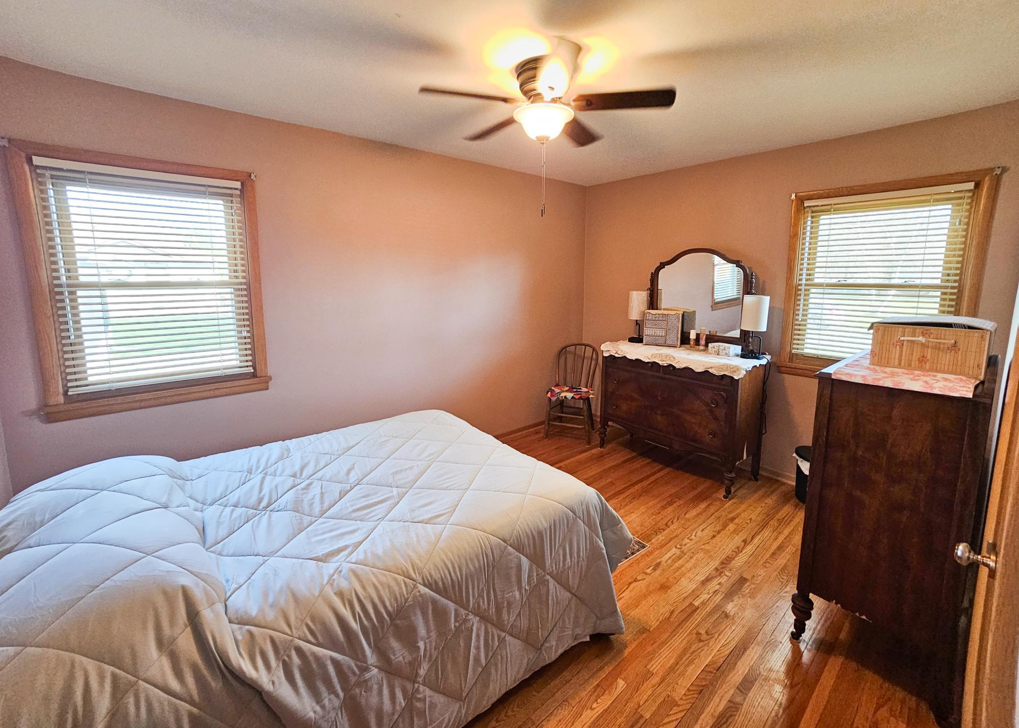 The second bedroom features a ceiling fan, multiple windows that create a bright, airy, atmosphere