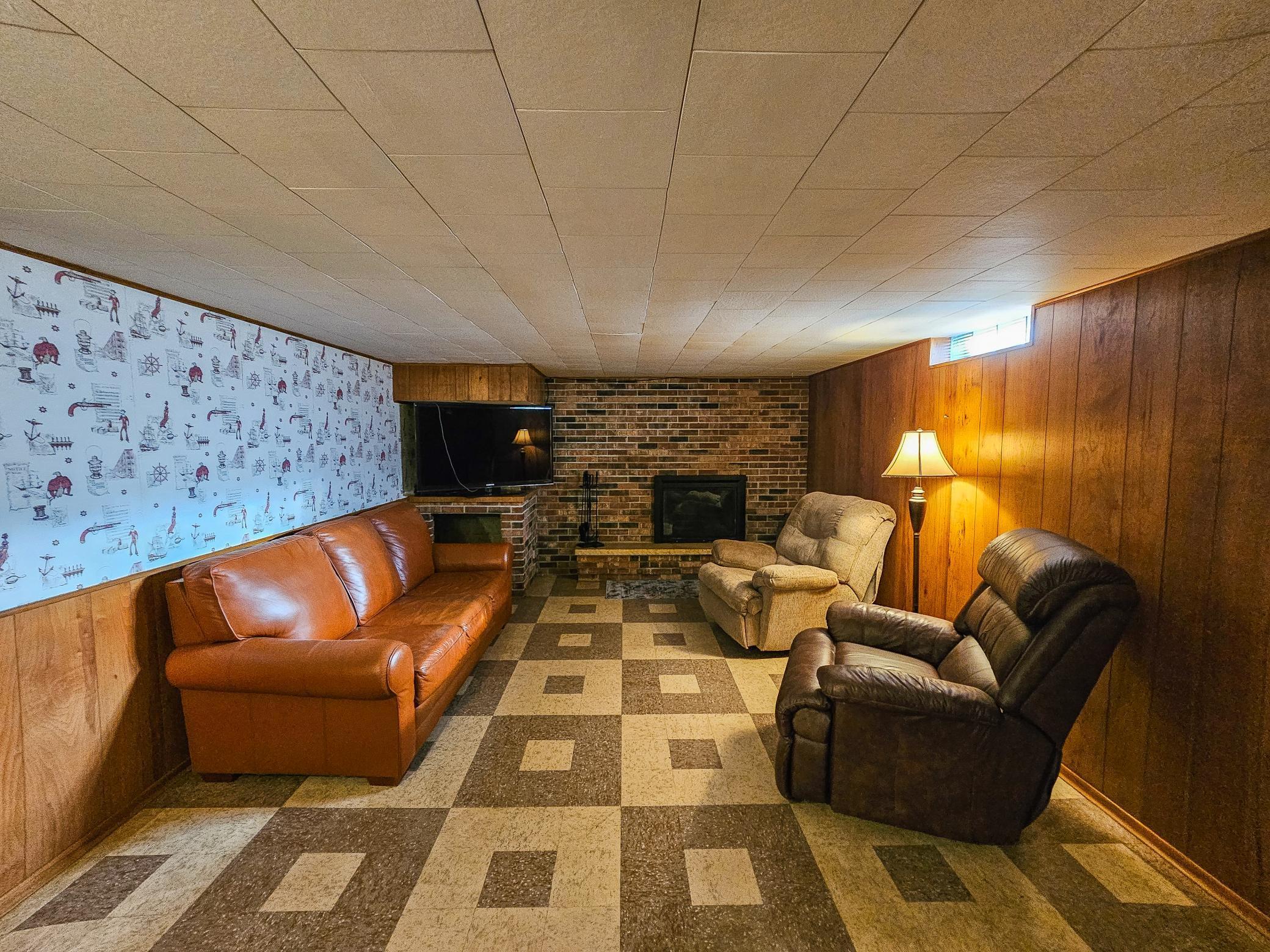 The finished basement showcases a nostalgic atmosphere with classic brick fireplace, and vintage wall covering.