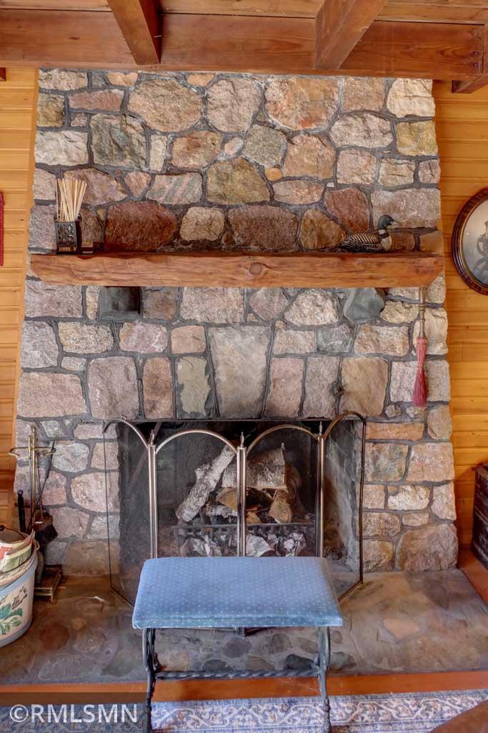 Large stone surrounds the wood burning fireplace in the living room.