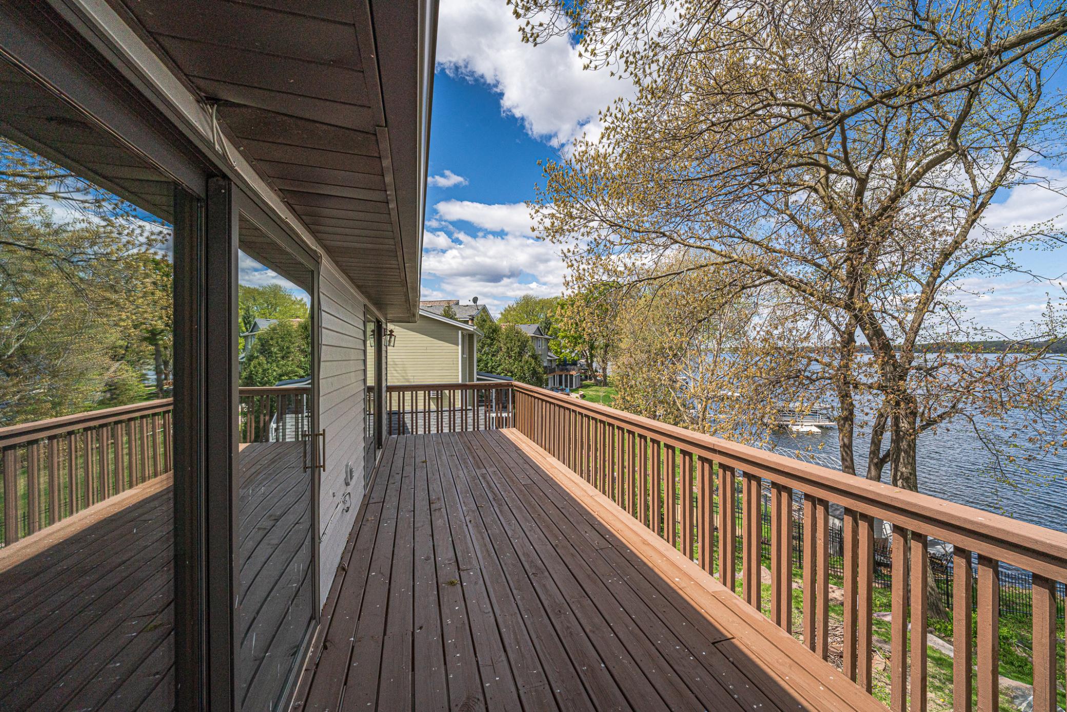 The upper level deck connects to both the primary suite and a second bedroom. It runs the length of the house and has panoramic lake views.