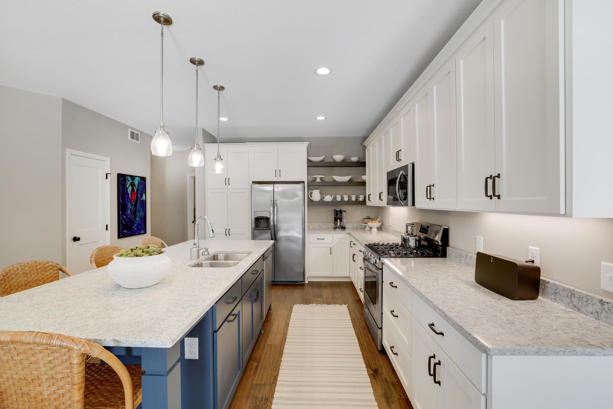 White cabinetry, stainless steel appliances, quartz countertops, elegant lighting, a gas range and decorative yet functional shelving make this kitchen absolutely perfect.