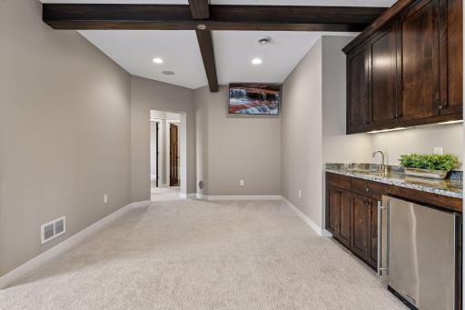 Family room wet bar area comes equipped with cabinetry, beverage refrigerator, and distinctive wood-beamed ceiling.