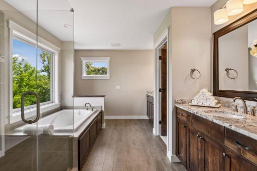 Spa-inspired primary bath with soaking tub, glass-enclosed shower, double vanity, and serene treetop and lake views.