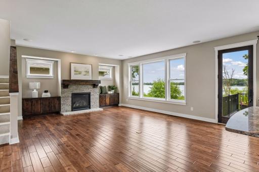 Great room with rich hardwood floors, oversized windows, and a stone-surround gas fireplace with custom built-ins.