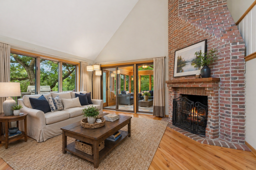 Inviting living room with vaulted ceilings, hardwood floors, brick wood-burning fireplace, and seamless access to the four-season porch.This photo has been virtually staged.
