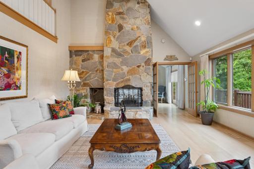 Dramatic great room featuring soaring ceilings, expansive windows, and a stunning natural fieldstone wood-burning fireplace.
