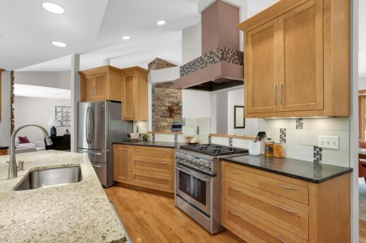 A closer view of the chef-inspired kitchen with stainless appliances and a 6 burner stove; the pass thru is open to the dining room with fireplace.